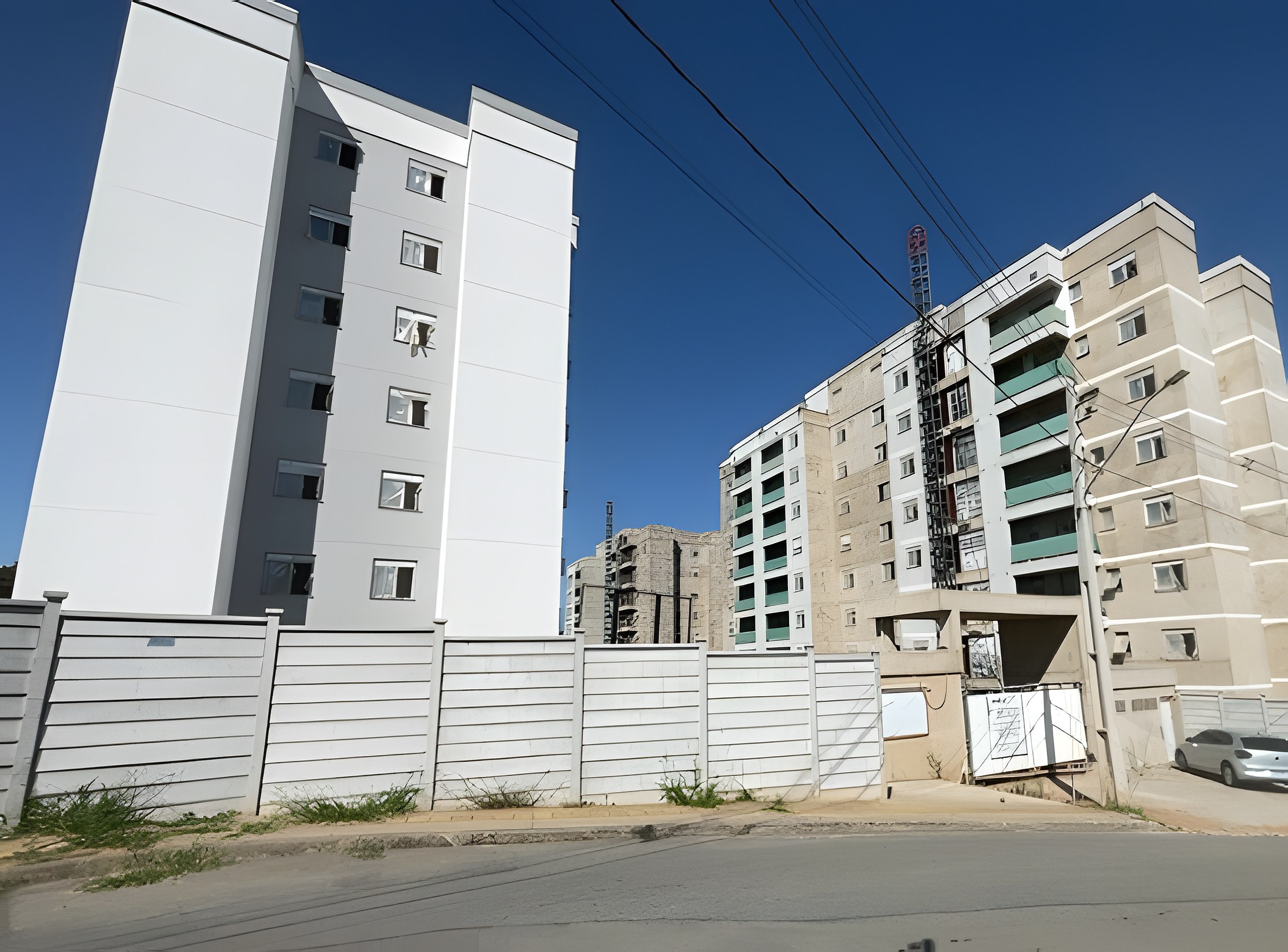 Torres residenciais em etapas distintas de obra: uma concluída e outra em revestimento de fachada, com elevador de cremalheira e muro em placas pré-moldadas